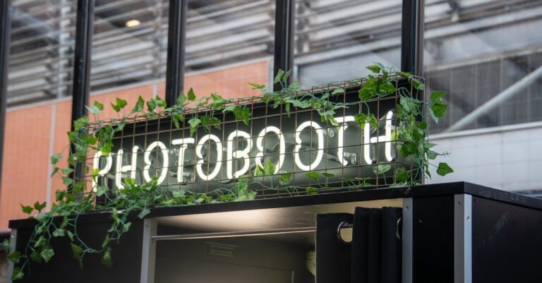 A contemporary photobooth with neon sign and greenery, set outdoors.