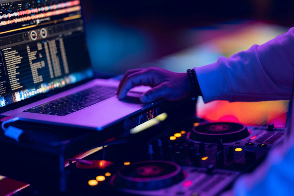 DJ adjusts music mix using laptop and mixer in vibrant nightclub setting.