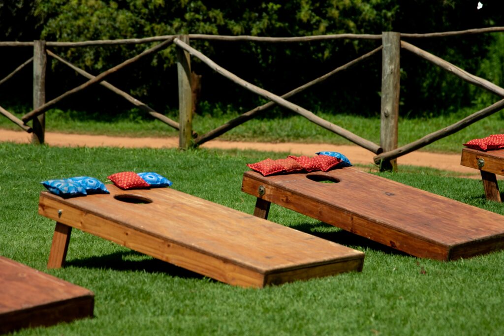 Wooden cornhole boards with colorful bean bags on a green lawn during a sunny day outdoors.